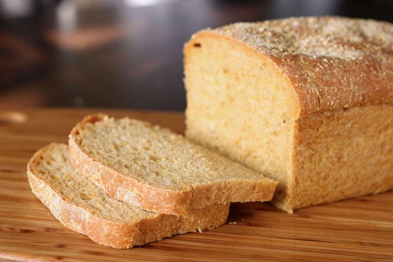 A loaf of anadama bread resting on a wooden cutting board, showcasing its rustic texture and golden-brown crust