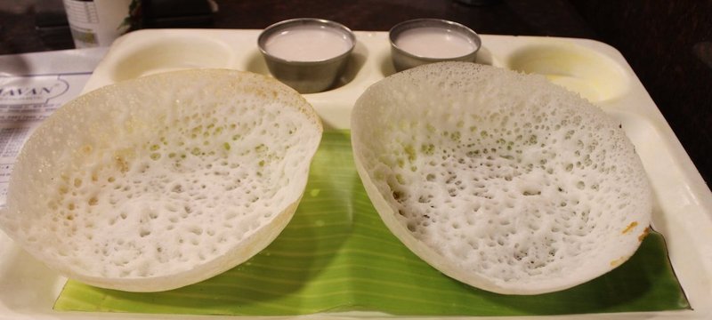Two Appam pancakes served with coconut milk arranged neatly on a tray