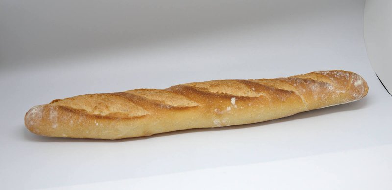 A baguette resting on a white surface, showcasing its long shape and crusty exterior