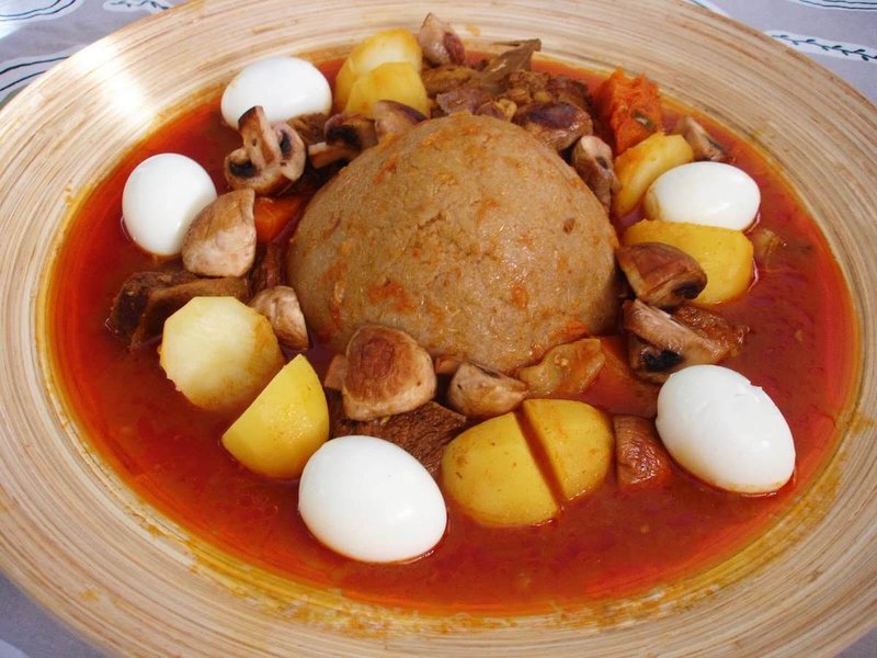 A plate of Bazin (center) served with a stew and whole hard-boiled eggs