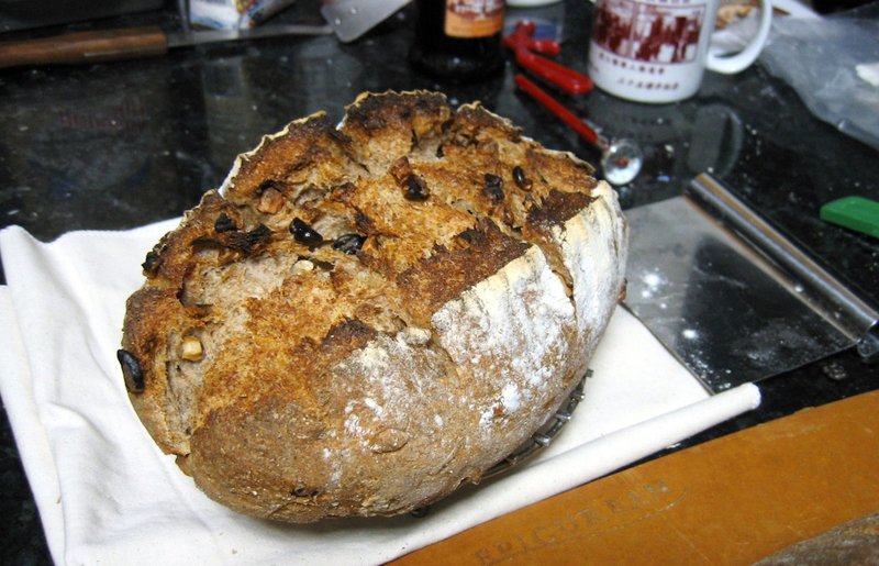 A loaf of sourdough rye with walnuts resting on a napkin atop a kitchen counter